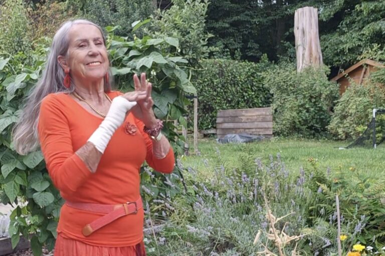 Marion Timmers, kunstenares, dansend in een oranje jurk in haar moestuin